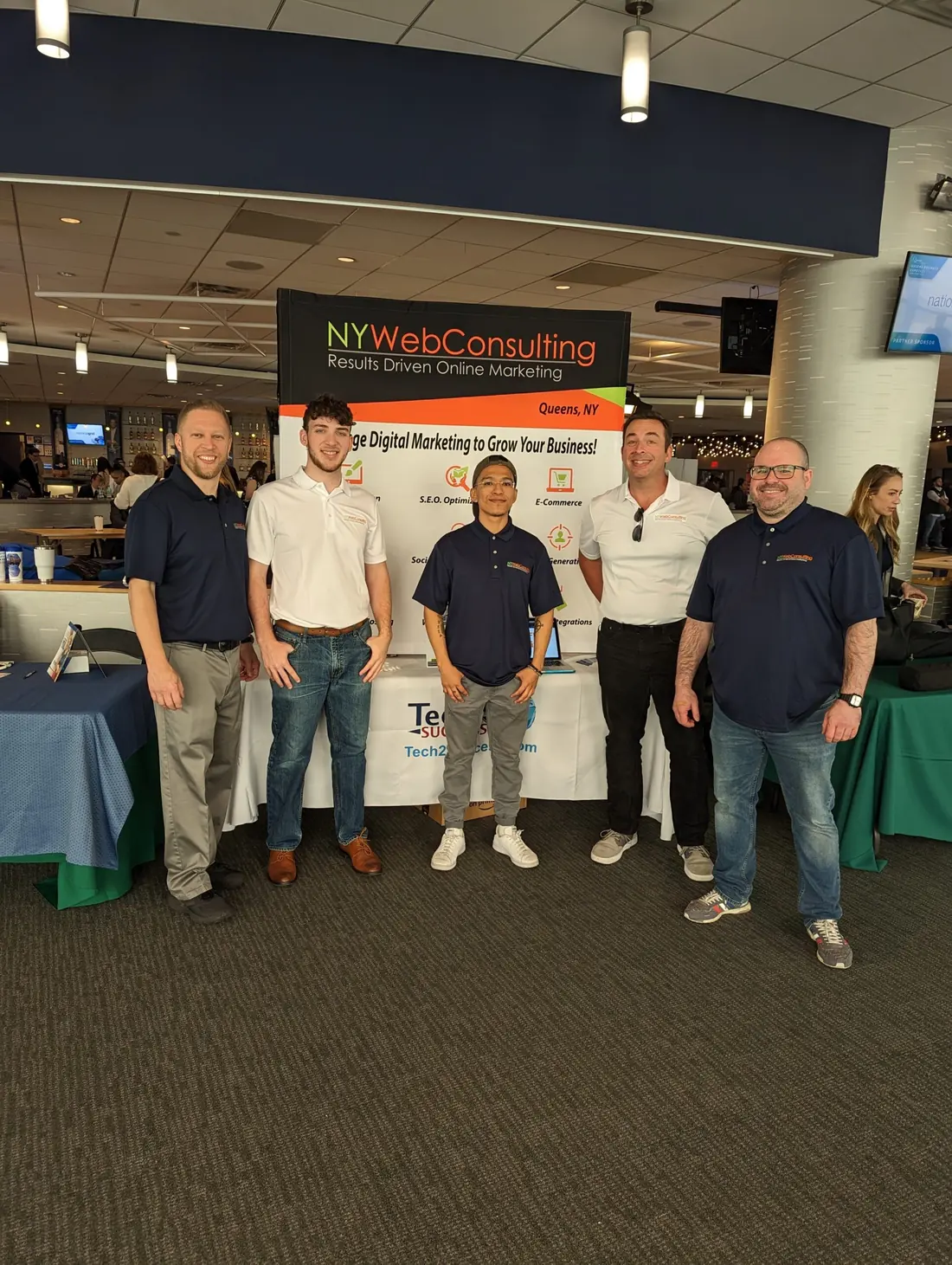 Five NY Web Consulting team members at an event with the company banner